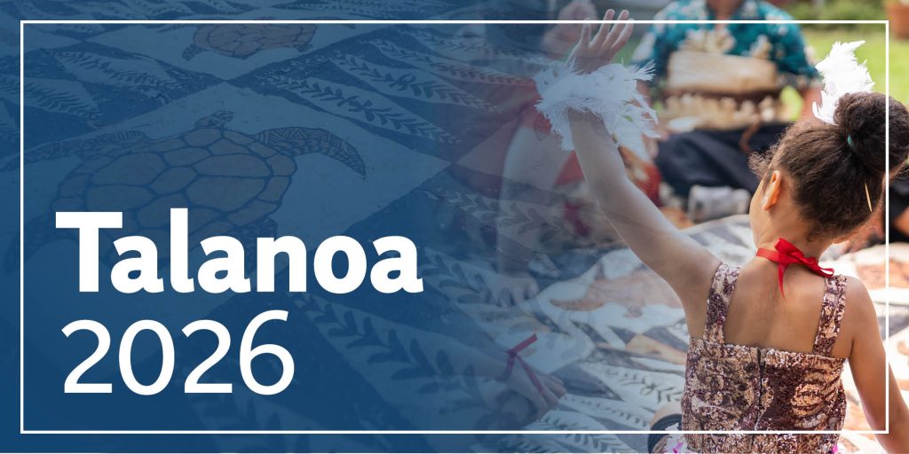 A young girl in traditional Tongan attire sits in a circle with her family, raising her hand. Beside her lies a patterned cloth decorated with turtle motifs.